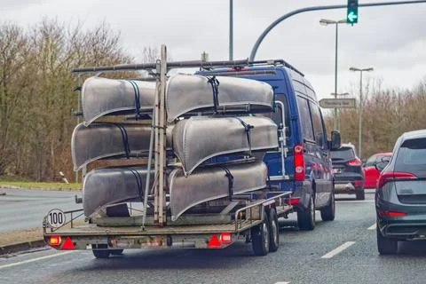 Van towing trailer loaded with multiple metal canoes on a city road Stock Photos