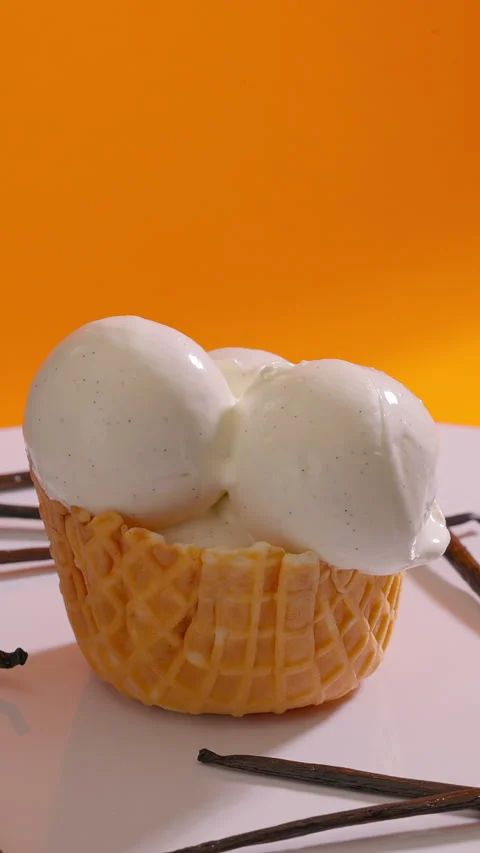 Vanilla ice cream scoops with vanilla seeds stacked into waffle cone surrounded Stock Footage 314132990
