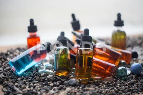 Vape concept. Beautiful colorful vape liquid glass bottles outdoor on stones. Stock Photos
