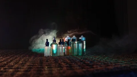 Vape concept. Smoke clouds and vape liquid bottles at dark background.