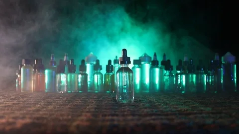 Vape concept. Smoke clouds and vape liquid bottles at dark background.