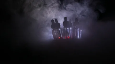 Vape concept. Smoke clouds and vape liquid bottles at dark background.