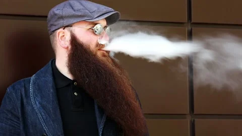 Vape man. Bearded man in a cap and sunglasses smokes an electronic cigarette. Stock Footage 107984448