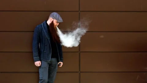 Vape man. Bearded man in a cap and sunglasses smokes an electronic cigarette. Stock Footage 107984457