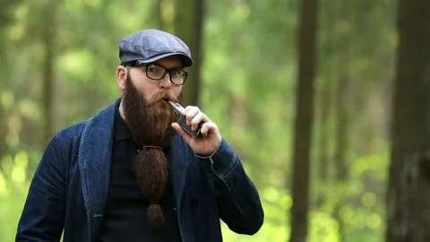 Vape man. Bearded man in a cap and glasses smokes an electronic cigarette. Stock Footage 107984510
