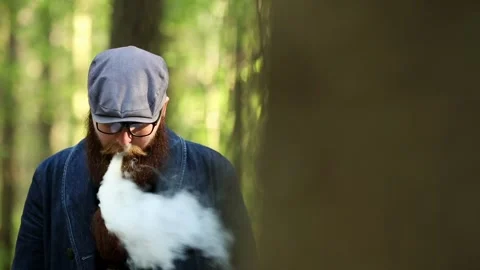 Vape man. Bearded man in a cap and glasses smokes an electronic cigarette. Stock Footage 107984614