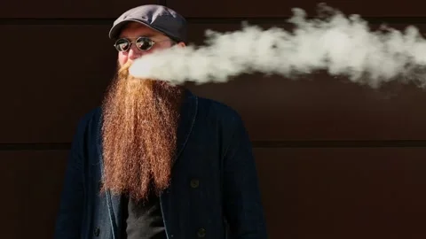 Vape man. Bearded man in a cap and sunglasses smokes an electronic cigarette. Stock Footage 108468179