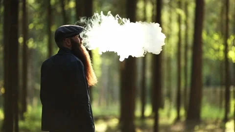 Vape man. Bearded man in a cap and glasses smokes an electronic cigarette. Stock Footage 108468198