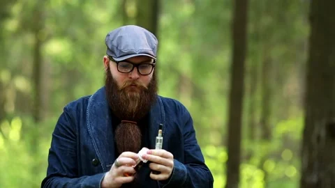 Vape man. Bearded man in a cap and glasses smokes an electronic cigarette. Stock Footage 108468250