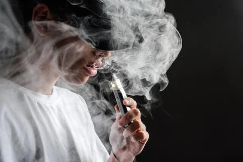 Vaper Exhaling Smoke from an E-Cigarette in a Dark Setting Stock Photos