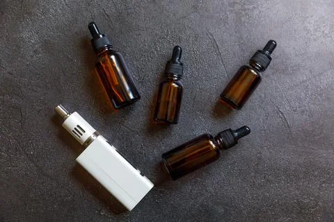 Vaping device e-cigarette electronic cigarette and liquid bottles on dark b.. Stock Photos