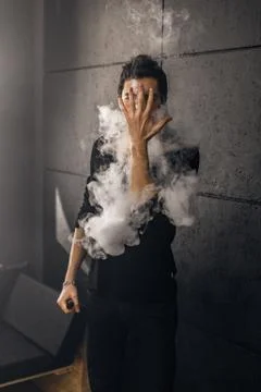 Vaping man holding a mod. A cloud of vapor. Black background Stock Photos