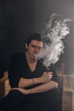 Vaping man holding a mod. A cloud of vapor. Black background Foto stock