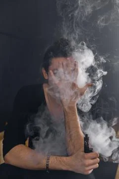 Vaping man holding a mod. A cloud of vapor. Black background Stock Photos