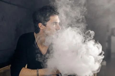 Vaping man holding a mod. A cloud of vapor. Black background Stock Photos