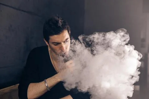 Vaping man holding a mod. A cloud of vapor. Black background Stock Photos