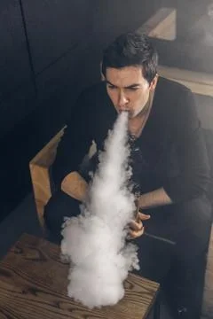 Vaping man holding a mod. A cloud of vapor. Black background 스톡 사진