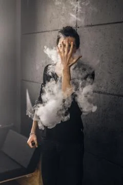 Vaping man holding a mod. A cloud of vapor. Black background Stock-Fotos