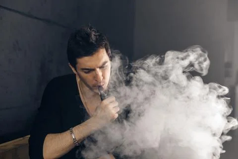 Vaping man holding a mod. A cloud of vapor. Black background Stock Photos