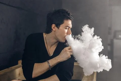 Vaping man holding a mod. A cloud of vapor. Black background Foto stock
