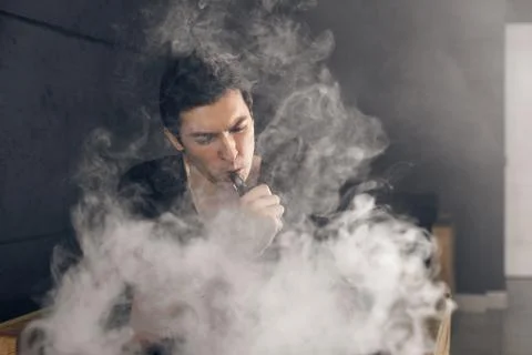 Vaping man holding a mod. A cloud of vapor. Black background Stock-Fotos