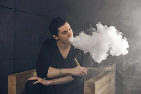 Vaping man holding a mod. A cloud of vapor. Black background Stock Photos