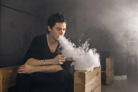 Vaping man holding a mod. A cloud of vapor. Black background Stock Photos
