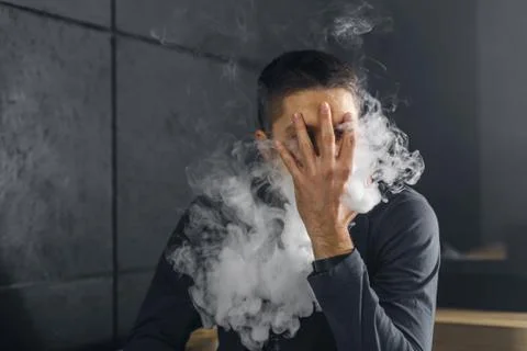 Vaping man holding a mod. A cloud of vapor. Black background Stock-Fotos