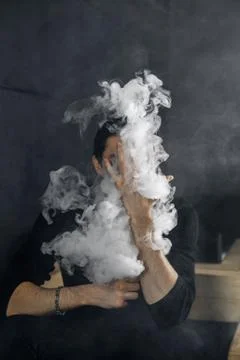 Vaping man holding a mod. A cloud of vapor. Black background Stock Photos
