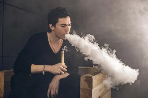 Vaping man holding a mod. A cloud of vapor. Black background Stock-Fotos