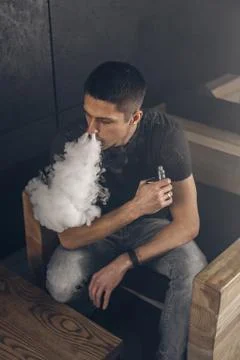 Vaping man holding a mod. A cloud of vapor. Black background Stock Photos