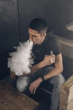 Vaping man holding a mod. A cloud of vapor. Black background Foto stock