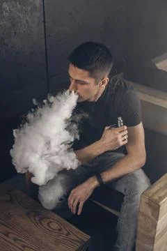 Vaping man holding a mod. A cloud of vapor. Black background 스톡 사진