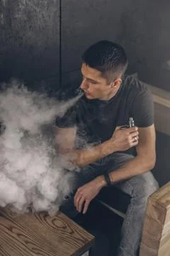Vaping man holding a mod. A cloud of vapor. Black background Stock Photos