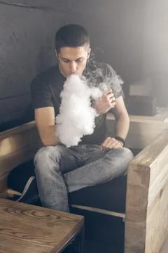 Vaping man holding a mod. A cloud of vapor. Black background Stock Photos