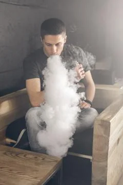 Vaping man holding a mod. A cloud of vapor. Black background Foto stock