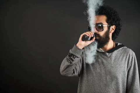 Vaping man holding a mod. A cloud of vapor. Black background. Vaping an Stock Photos
