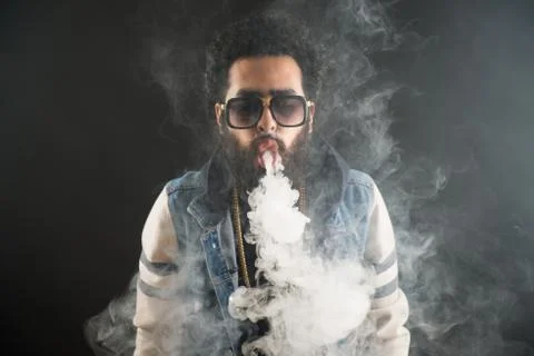 Vaping man holding a mod. A cloud of vapor. Black background. Vaping an Stock Photos