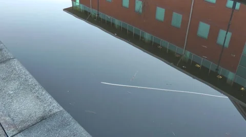 Vapour trail modern office block reflected in canal - pan up aircraft in sky Stock Footage 1058000
