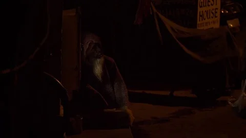 VARANASI, India - elderly man sat huddled beside small pavement shrine at prayer Video stock 85396259