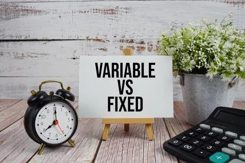 Variable vs Fixed text with alarm clock and calculator on wooden background Stock-Fotos