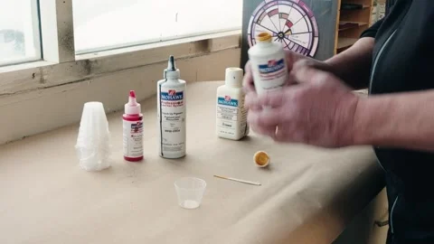 Varied paint bottles line window-lit bench as hands blend custom hue inside a Stock Footage 309105495