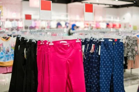 Variety of bright colour and patterns jeans on hangers in kids clothes store Stock Photos
