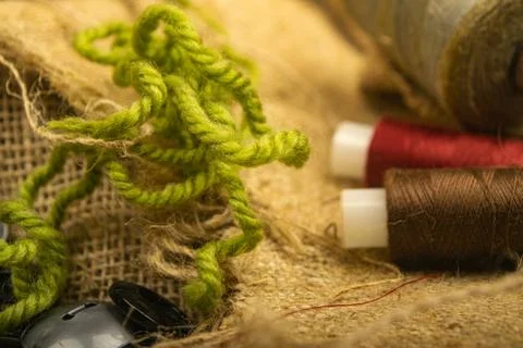 Various buttons and multicolored threads on coarse-textured burlap. Close up. Stock Photos
