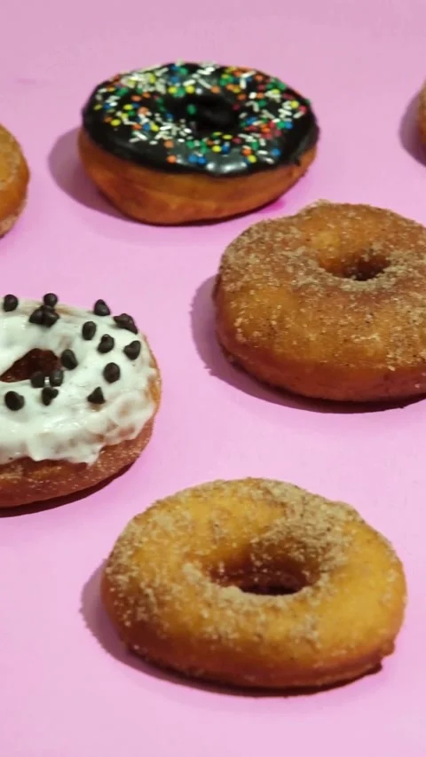 Various colorful donuts displayed on a bright pink background Stock Footage 331780975