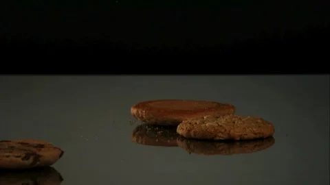 Various cookies fall and tumble on a dark reflective floor. Stock Footage 326747940