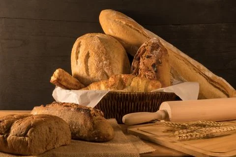 Various crusty bread in wicker basket, wheat  and wooden rolling pin on rus.. Stock Photos