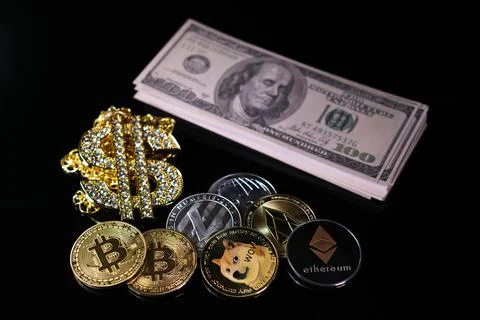 Various crypto coins lie next to a stack of 100-dollar bills, a white alarm c Stock Photos