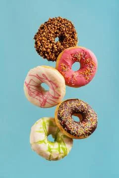 Various decorated doughnuts in motion falling on blue background. Stock Photos