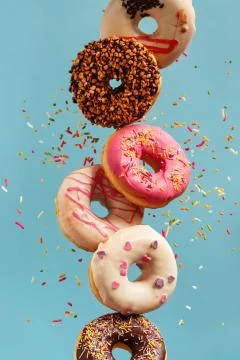 Various decorated doughnuts in motion falling on blue background. Stock Photos